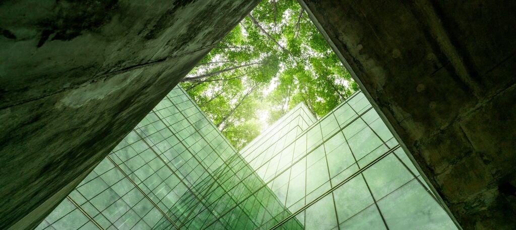 Modern glass office building surrounded by trees, symbolising sustainable business, environmental responsibility and corporate sustainability.