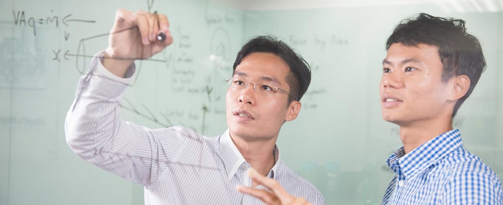 Two people discussing maths writing on glass