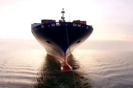 A cargo ship loaded with containers sits calmly on the water at sunrise, representing global maritime logistics.