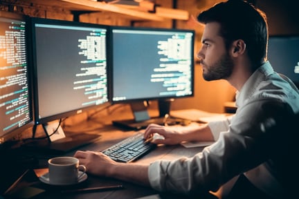 A developer sitting down working on code with two screens