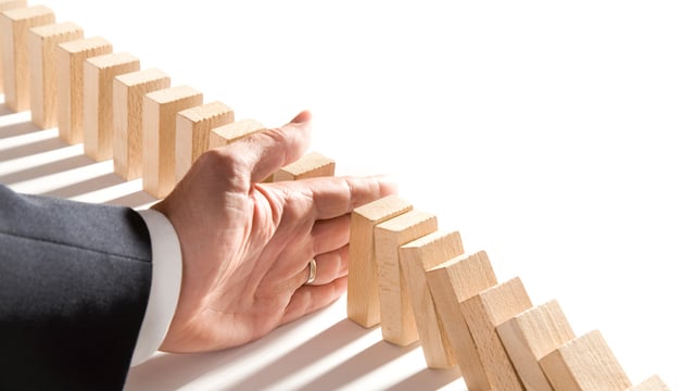 Hand of a businessman stopping the chain of falling dominoes