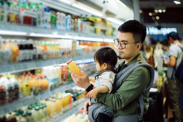 Hombre sosteniendo a su bebé mientras realiza compras de supermercado