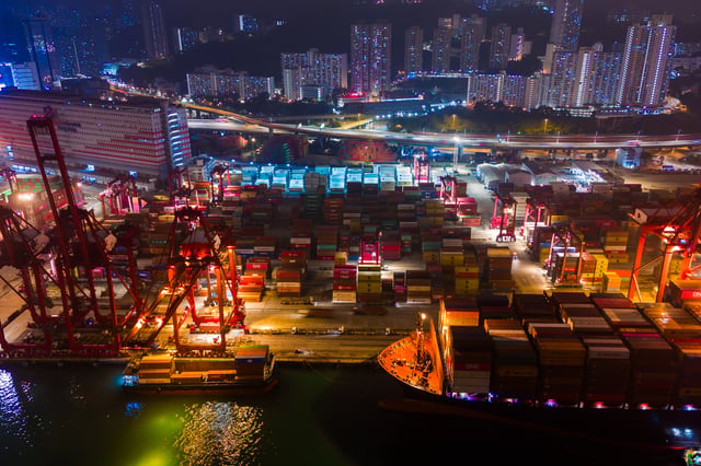 Vista aérea noturna de porto com contêineres, navios e operações logísticas em grande escala